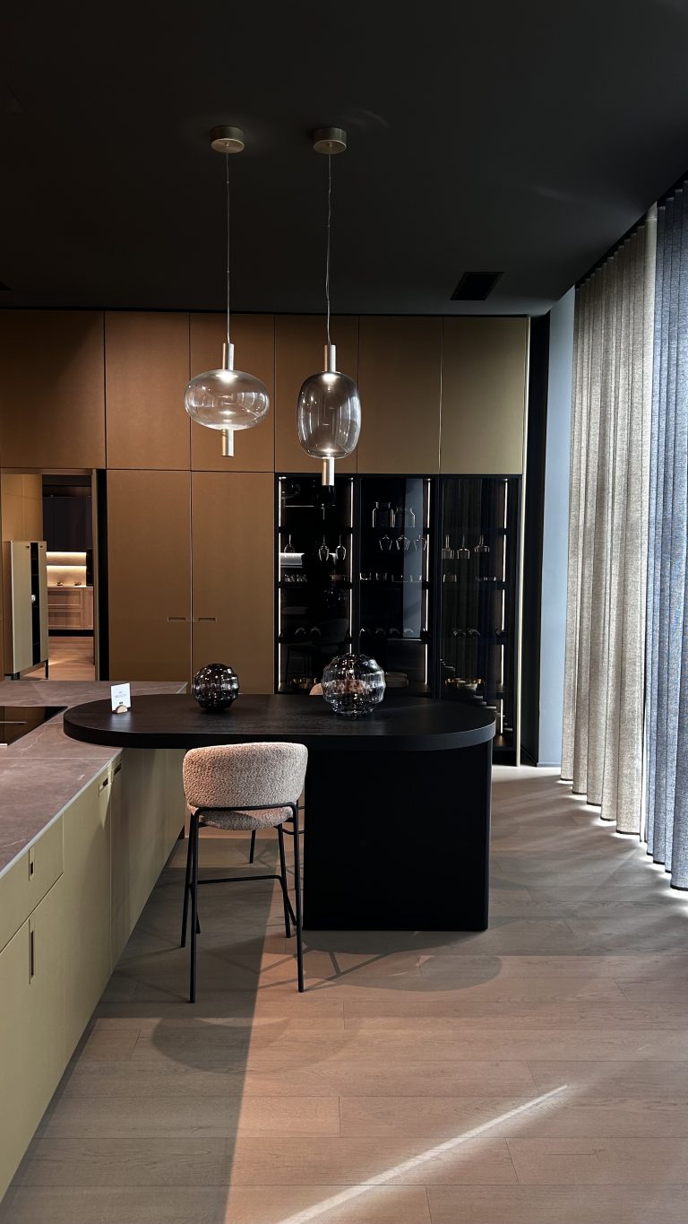 Découvrez une cuisine qui allie fonctionnalité et esthétisme, invitant à la convivialité. Les façades aux tons chauds et les détails dorés créent une atmosphère luxueuse et accueillante. L'espace bar élégant, parfait pour les moments de partage, est mis en valeur par des luminaires suspendus au design délicat. Le meuble vitrine noir, clin d'œil à l'esprit "Lago Air Kitchen", offre une vitrine sophistiquée pour votre vaisselle ou vos objets de collection. Chaque élément est pensé pour créer une ambiance intemporelle et distinguée.